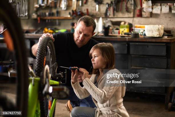 father and daughter repairing bicycle together in a workshop - bicycle daughter stock-fotos und bilder
