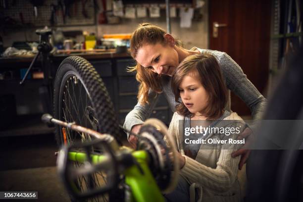 mother and daughter repairing bicycle together in a workshop - bicycle daughter stock-fotos und bilder