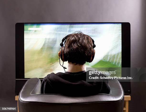 teenage boy sits in front of tv playing video game - boy headphones stock-fotos und bilder