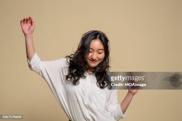 a young asian girl is listening to music - sfondo beige foto e immagini stock