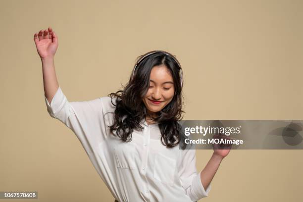 a young asian girl is listening to music - ベージュの背景 ストックフォトと画像