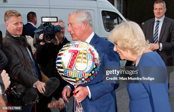 Camilla, Duchess of Cornwall looks on as Prince Charles, Prince of Wales receives a birthday present and helium balloon as they attends an Age UK...