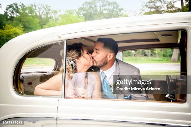 A latino bride and groom seen kissing through the window in a white car on their wedding day.