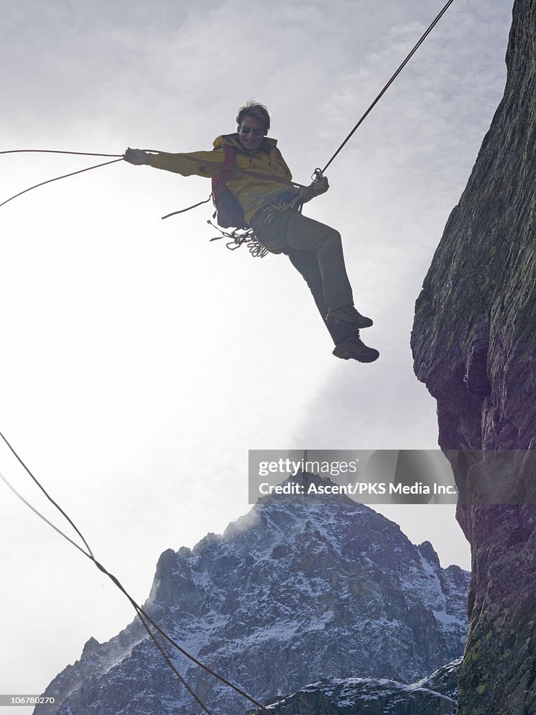 Climber rappels (abseils) cliff, mid-air jump