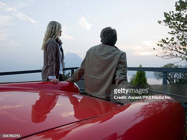 couple lean aginst hood of red sports car, relaxed - man lean car stock-fotos und bilder