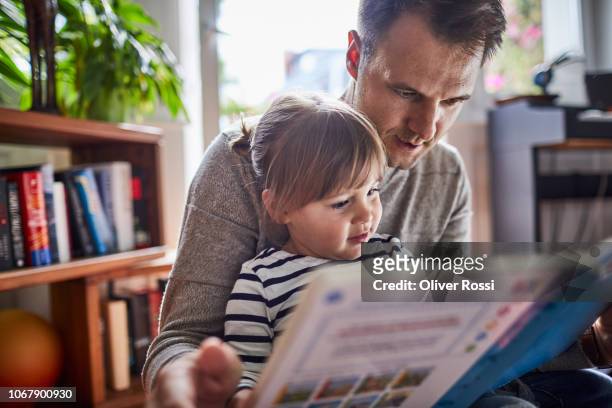 father reading book with daughter at home - reading stock-fotos und bilder