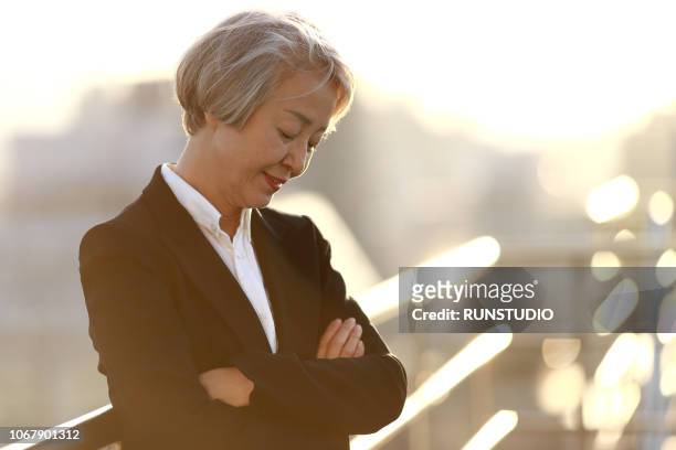 mature businesswoman standing with arms folded on rooftop - grey hair cool woman stock-fotos und bilder
