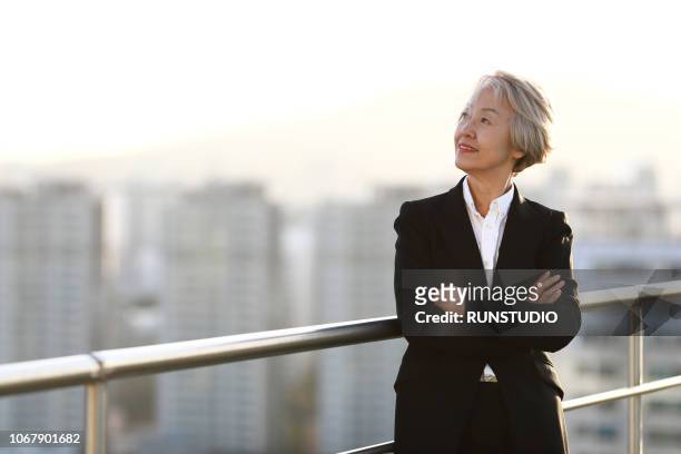 confident mature businesswoman standing with arms folded on rooftop - asian beauty face stock pictures, royalty-free photos & images