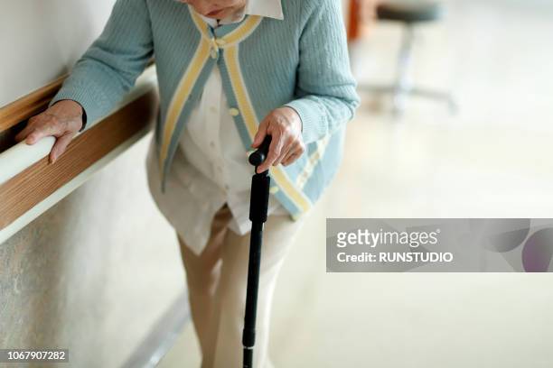 senior woman walking with walking cane in hospital corridor - spazierstock stock-fotos und bilder