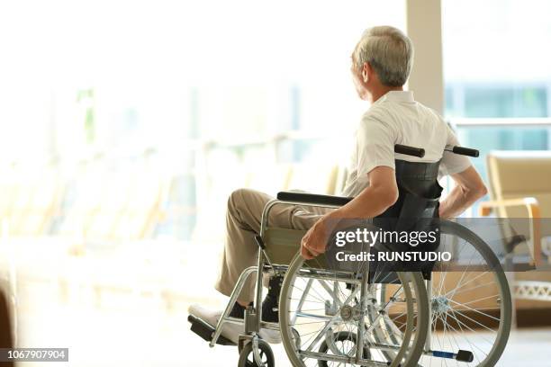 senior man in wheelchair looking out window - rolstoel stockfoto's en -beelden