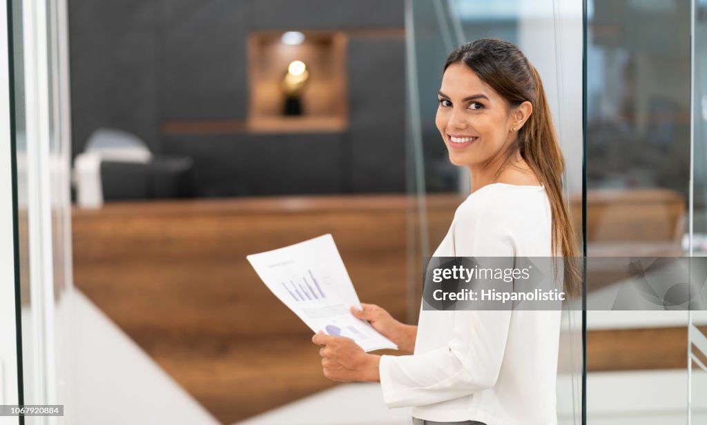 Empresária de latino-americanos confiante no escritório sorrindo para a câmera enquanto segura de documentos
