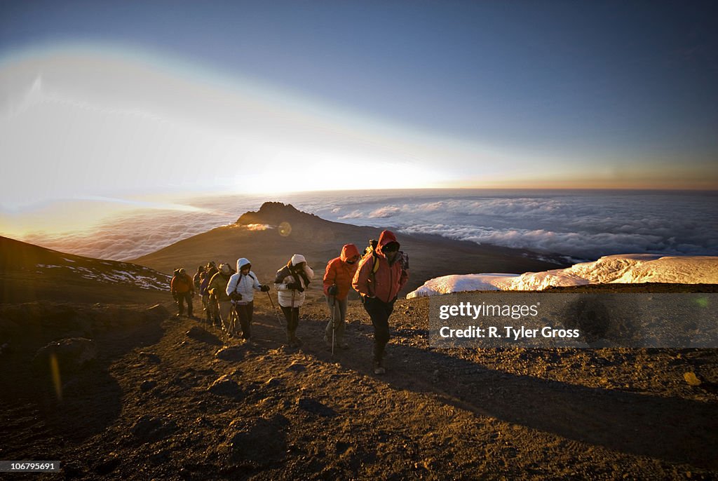 A team of hikers approach the summit of Mt. Kilimanjaro at sunrise after trekking six hours through the night.