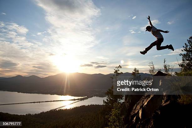 young man soaring at sunset next to a large cliff overlooking  a lake. - sandpoint stock pictures, royalty-free photos & images