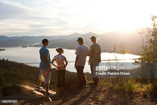 four young adult friends talk and take in the view after hiking at sunset. - sandpoint stock pictures, royalty-free photos & images