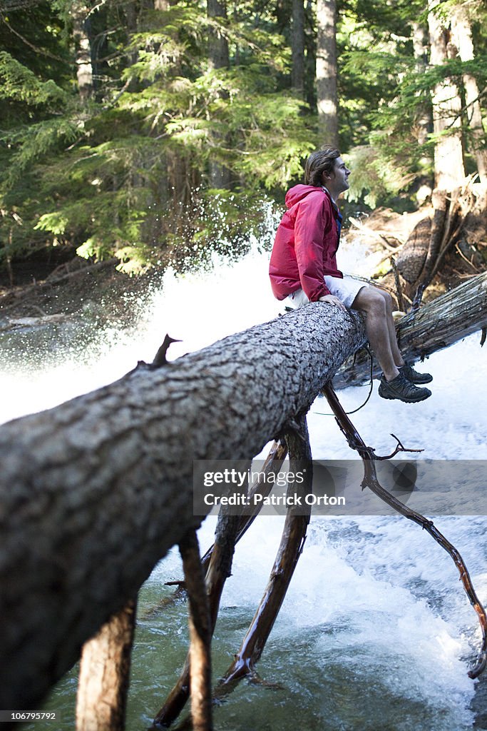 A young man sits on a log over a waterfall in Idaho.