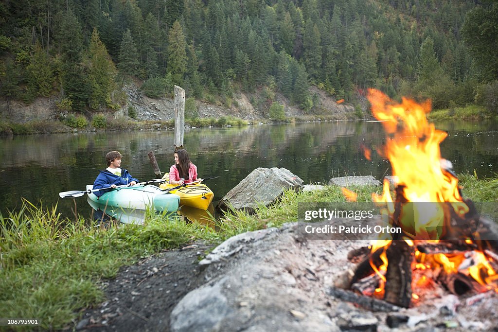 Young adult couple camping with a camp fire and kayaks on a beautiful summer evening.