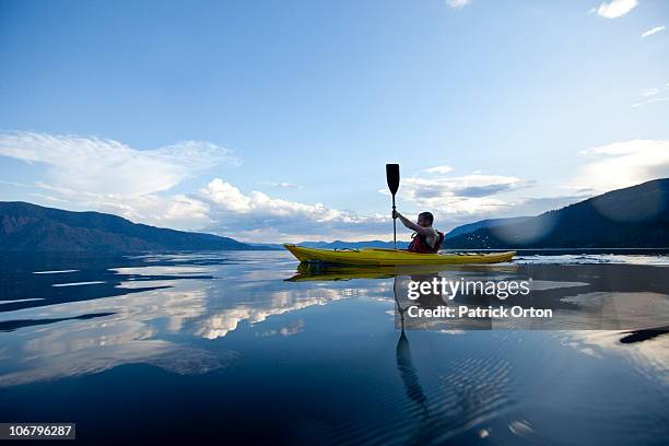 young man paddles yellow kayak on lake. - kayak stock-fotos und bilder