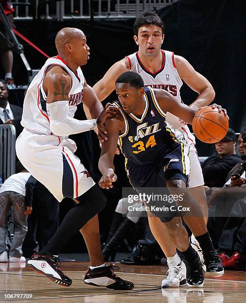 Miles of the Utah Jazz drives around Maurice Evans and Zaza Pachulia of the Atlanta Hawks at Philips Arena on November 12, 2010 in Atlanta, Georgia....