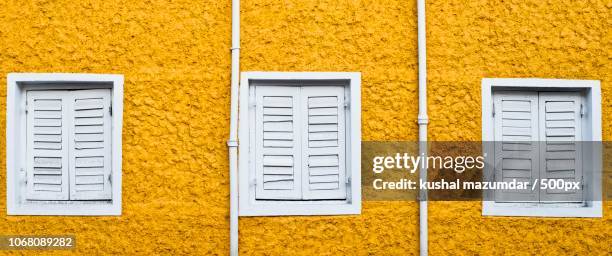 white windows with closed shutters in yellow wall - monochrome yellow stock pictures, royalty-free photos & images