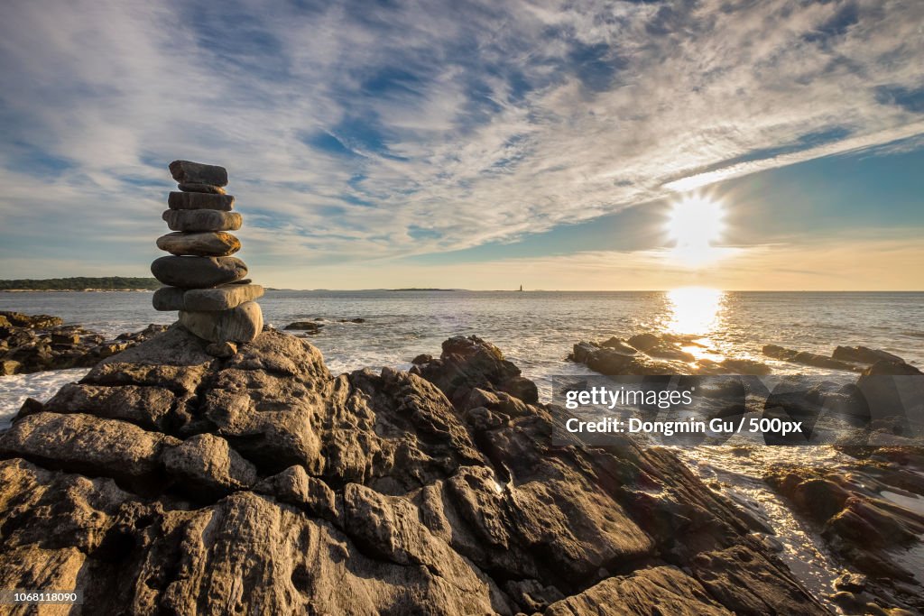 Scenic view of rocky coastline at sunrise with cairn stones