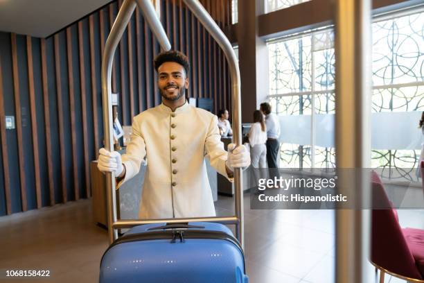 handsome black bellhop pushing cart with luggage at hotel - bell boy stock pictures, royalty-free photos & images