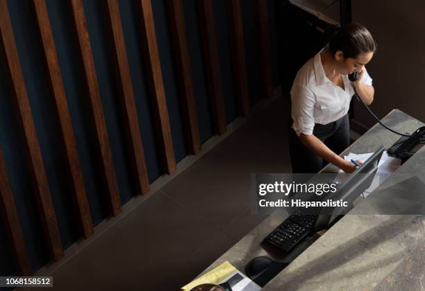 view from above of friendly receptionist taking a call from a guest at the hotel - concierge service stock pictures, royalty-free photos & images