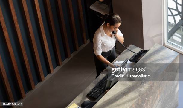 latin american hotel receptionist taking a phonecall - reception stock pictures, royalty-free photos & images