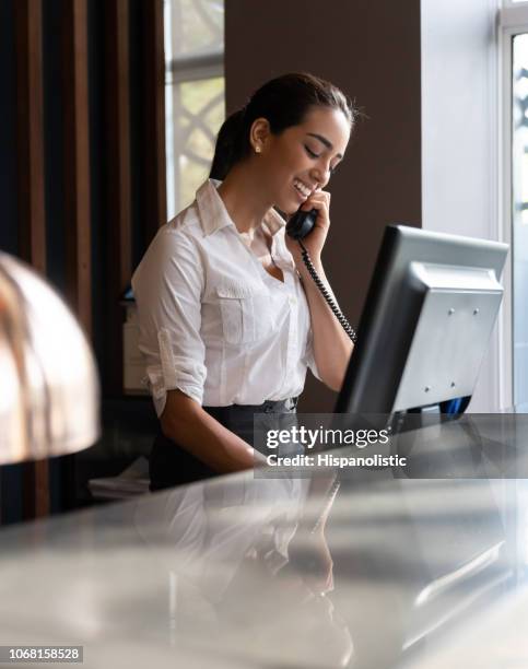 portret van mooie jonge receptioniste beantwoorden een phonecall bij de receptie glimlachen - concierge stockfoto's en -beelden