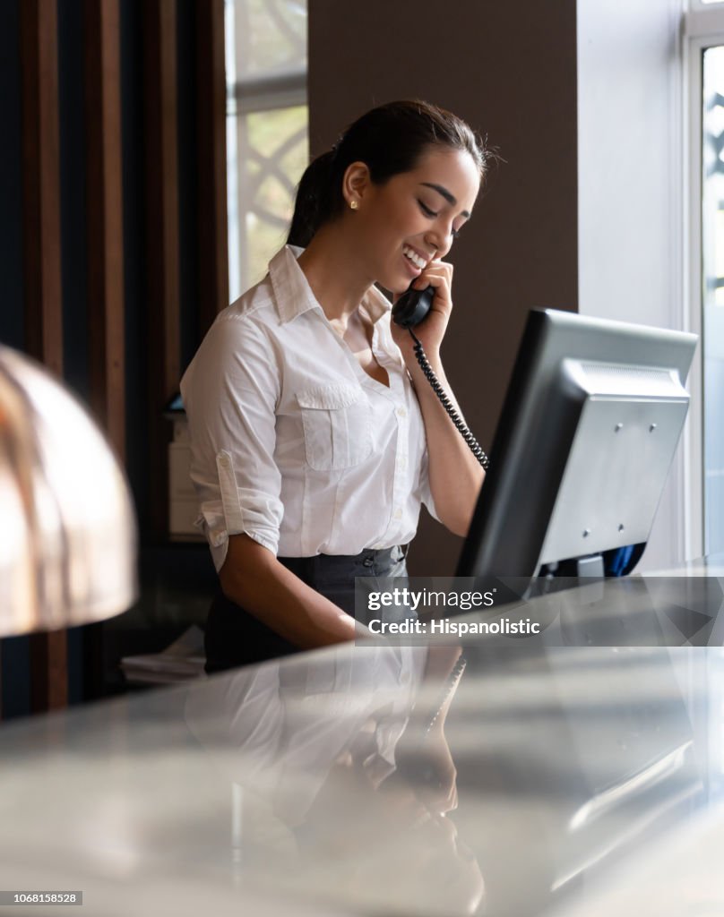 美麗的年輕接待員在前臺回答電話的肖像微笑