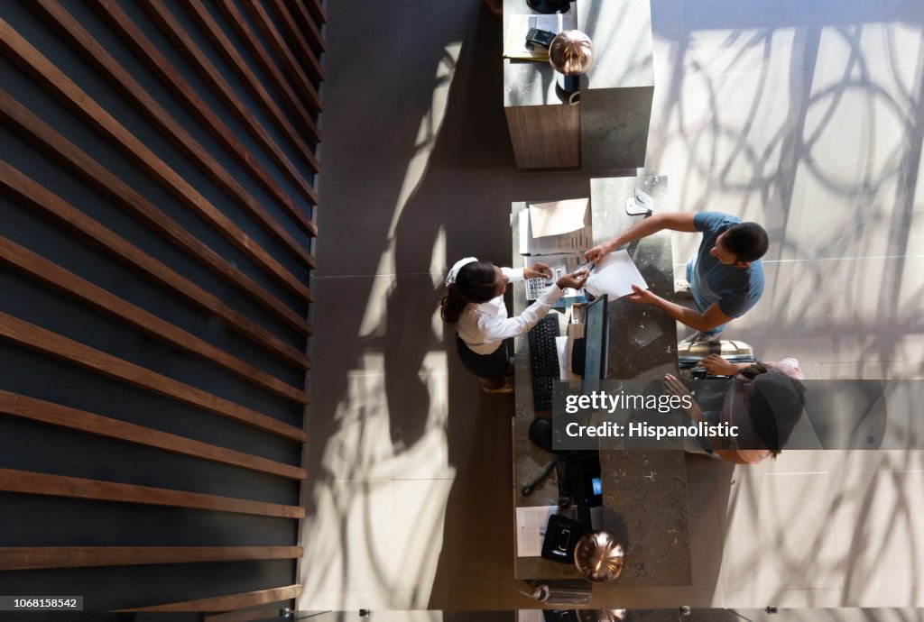 Amichevole receptionist nero che consegna un modulo agli ospiti maschi che fanno il check-in con il partner in un hotel di lusso