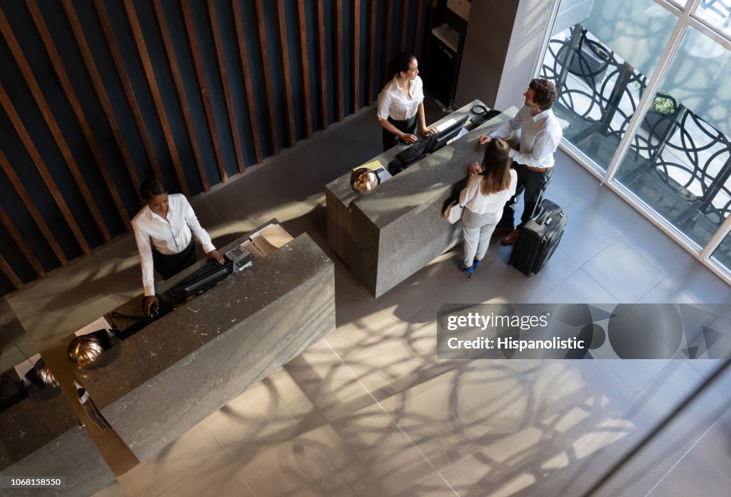 Young business couple checking in at hotel and beautiful receptionist helping them