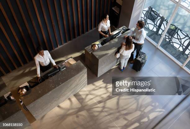 young business couple checking in at hotel and beautiful receptionist helping them - hotel stock pictures, royalty-free photos & images