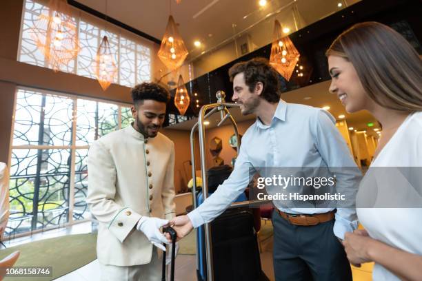 businessman with partner arriving to hotel and handing his bag to friendly bellhop - bellhop stock pictures, royalty-free photos & images