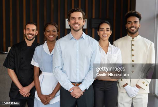 confident multi ethnic group of employees at a hotel reception all looking at camera smiling - hotel occupation stock pictures, royalty-free photos & images