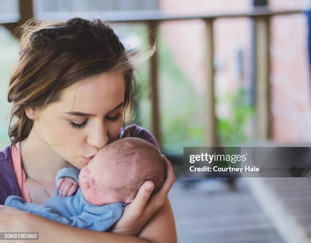 mutter neugeborenen sohn auf die wange küsst, als sie ihn hält - new mum stock-fotos und bilder