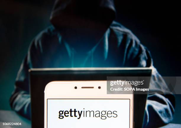 In this photo illustration, the American stock photo agency logo is seen displayed on an Android mobile device with a figure of hacker in the...