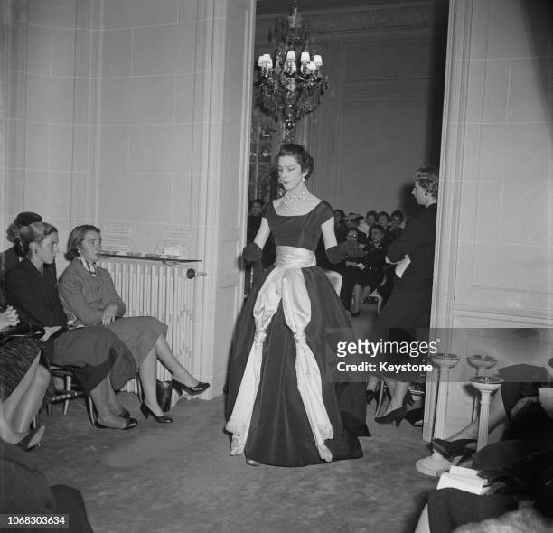 Model wearing an evening gown in black satin, decorated with two large, knotted scarves, at the Dior Salon in Paris, 17th October 1954. The event is...