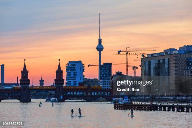 standup paddlers on spree river - with berlin skyline sunset at oberbaumbrücke and television-tower (kreuzberg-friedrichshain, berlin, germany) - river spree stock pictures, royalty-free photos & images