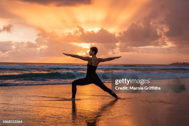 woman doing yoga on the beach at sunrise - sunrise yoga stock pictures, royalty-free photos & images