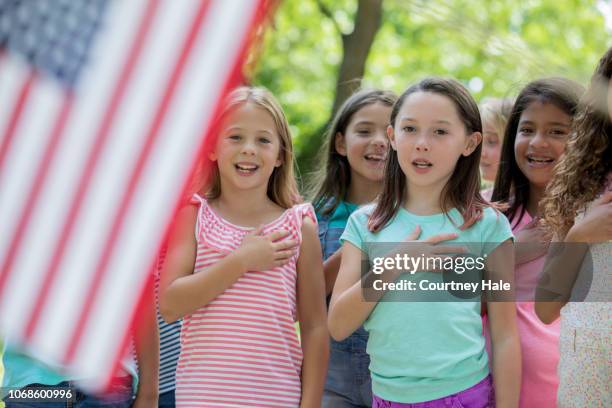 diverse group of elementary school age girls saying pledge of allegiance to the american flag outdoors - pledge of allegiance stock pictures, royalty-free photos & images
