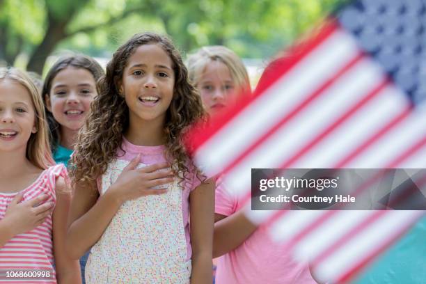 biracial elementare alter mädchen pledge of allegiance rezitieren, mit klassenkameraden im freien - amerikanischer treueschwur stock-fotos und bilder