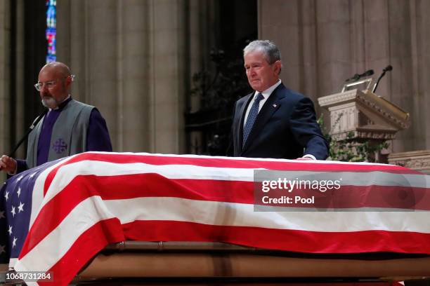 Former President George W. Bush touches the casket of his father, former President George H.W. Bush, at the State Funeral at the Washington National...