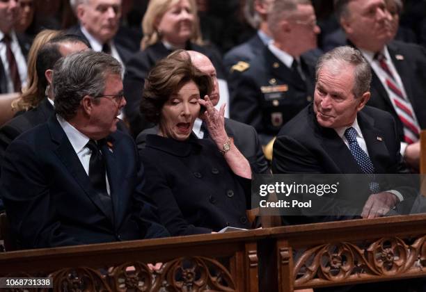 Former First Lady Laura Bush wipes her eye during a moment of levity as former President George W. Bush and his brother Jeb Bush look on during the...