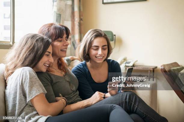 mother and daughters on sofa with smartphone - older sibling stock pictures, royalty-free photos & images