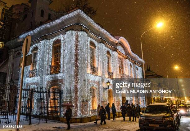Pedestrians walk under the snow in front of the famous restaurant "Café Pushkin" decorated with festive lights for the upcoming holidays in Moscow on...