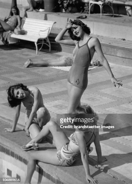 Three bathing beauties pose at the side of a swimming pool, wearing the bathing fashion of the time. Germany. Around 1940
