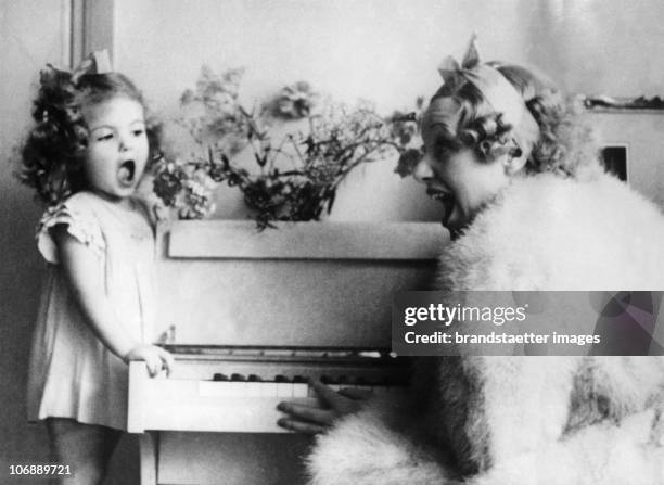 Originally hungarian singer Gitta Alpar at the piano singing with her two year old daughter Julika. Photograph. London. 1936.