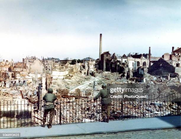 Two American soldiers stand behind a fence and survey the damage sustained during a saturation bombing raid on the city of Darmstadt, Germany, 1945....