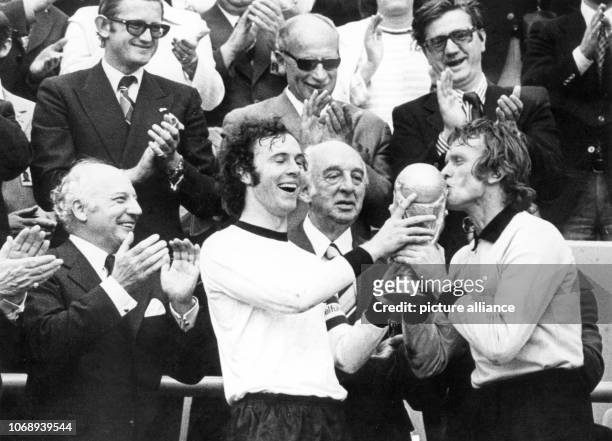 Laughing German captain Franz Beckenbauer and goalkeeper Sepp Maier hold the just won World Cup trophy with Maier even kissing it. On the left,...