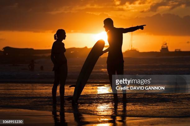 Surfer speaks to a woman as the sun sets in Tamarindo, Costa Rica on December 5, 2018.
